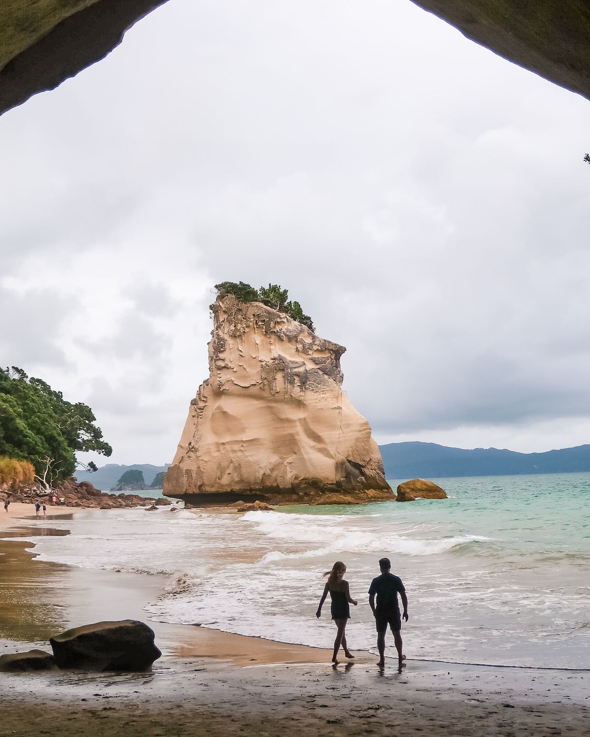 Cec and Ari walking with bare feet in the sand at Cathedral Cove, New Zealand