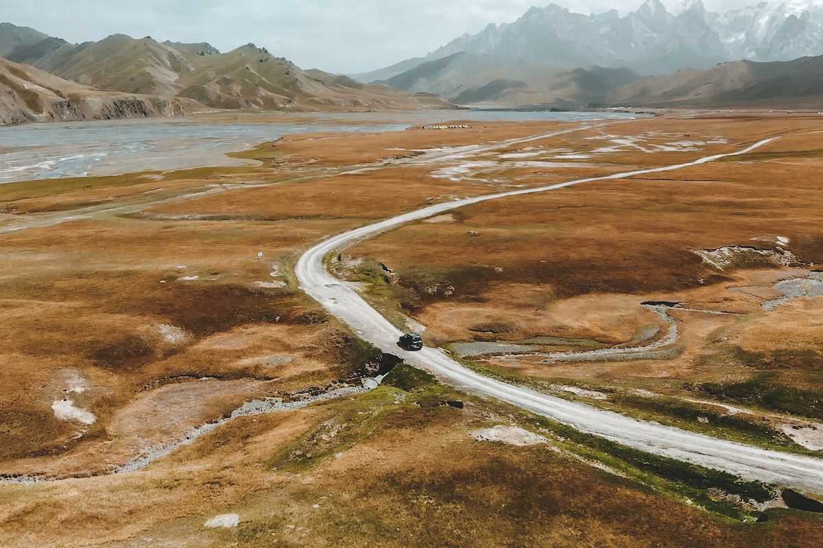 Lonely road winds through grassy plains in Kyrgyzstan toward the Tian Shan Mountains.