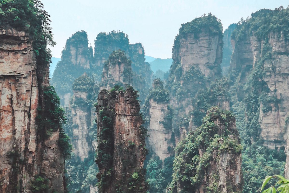 Towering sandstone pillars covered in green vegetation rise through mist at Zhangjiajie National Forest Park, China.