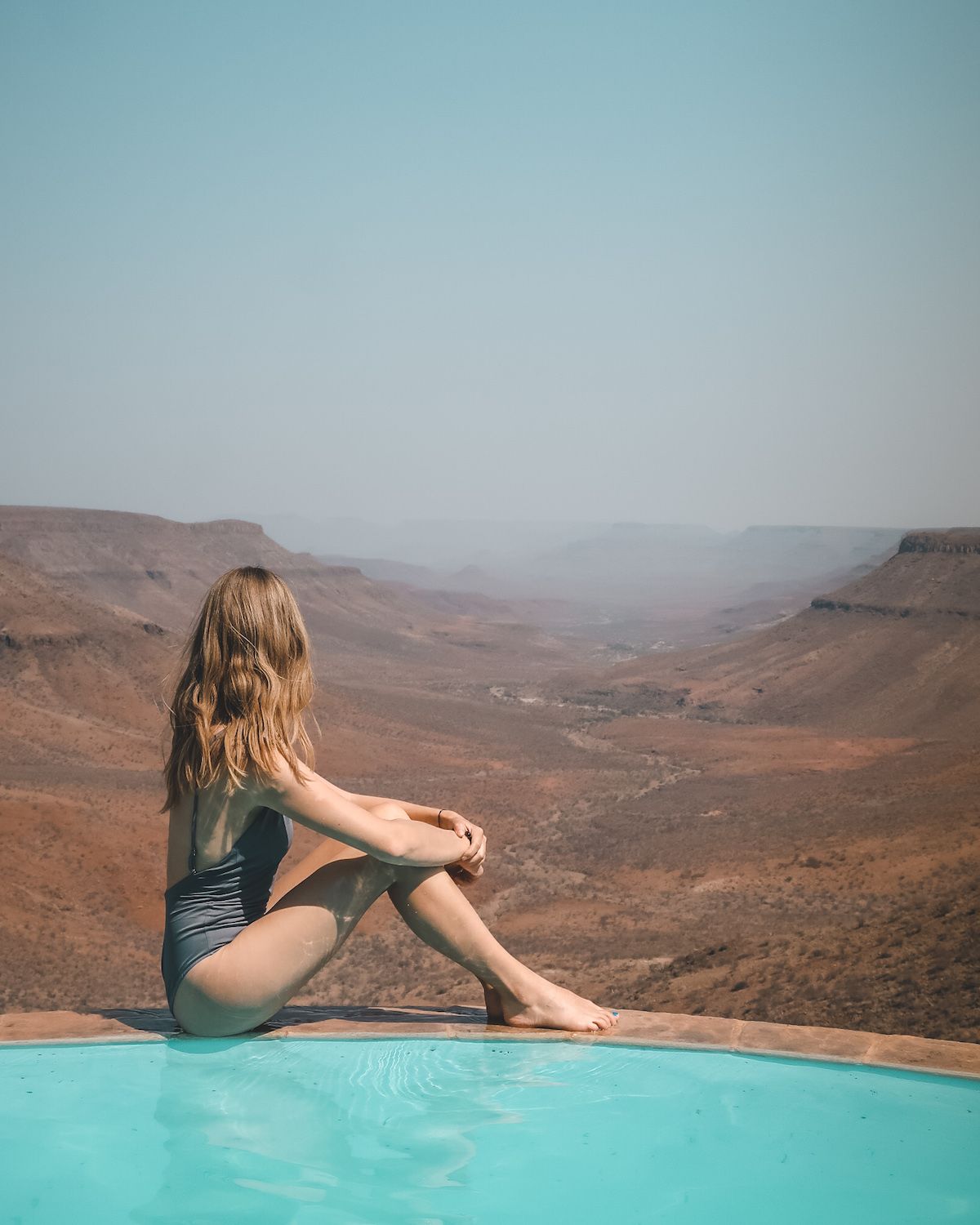 Cec sitting on the edge of an infinity pool overlooking Namibia's vast landscape 