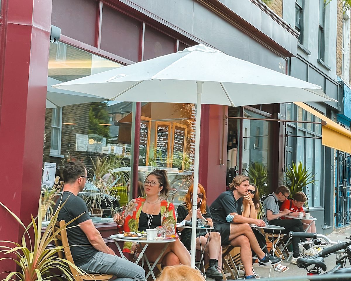 People sitting at small tables under umbrellas on Wilton Way, enjoying food and drinks.