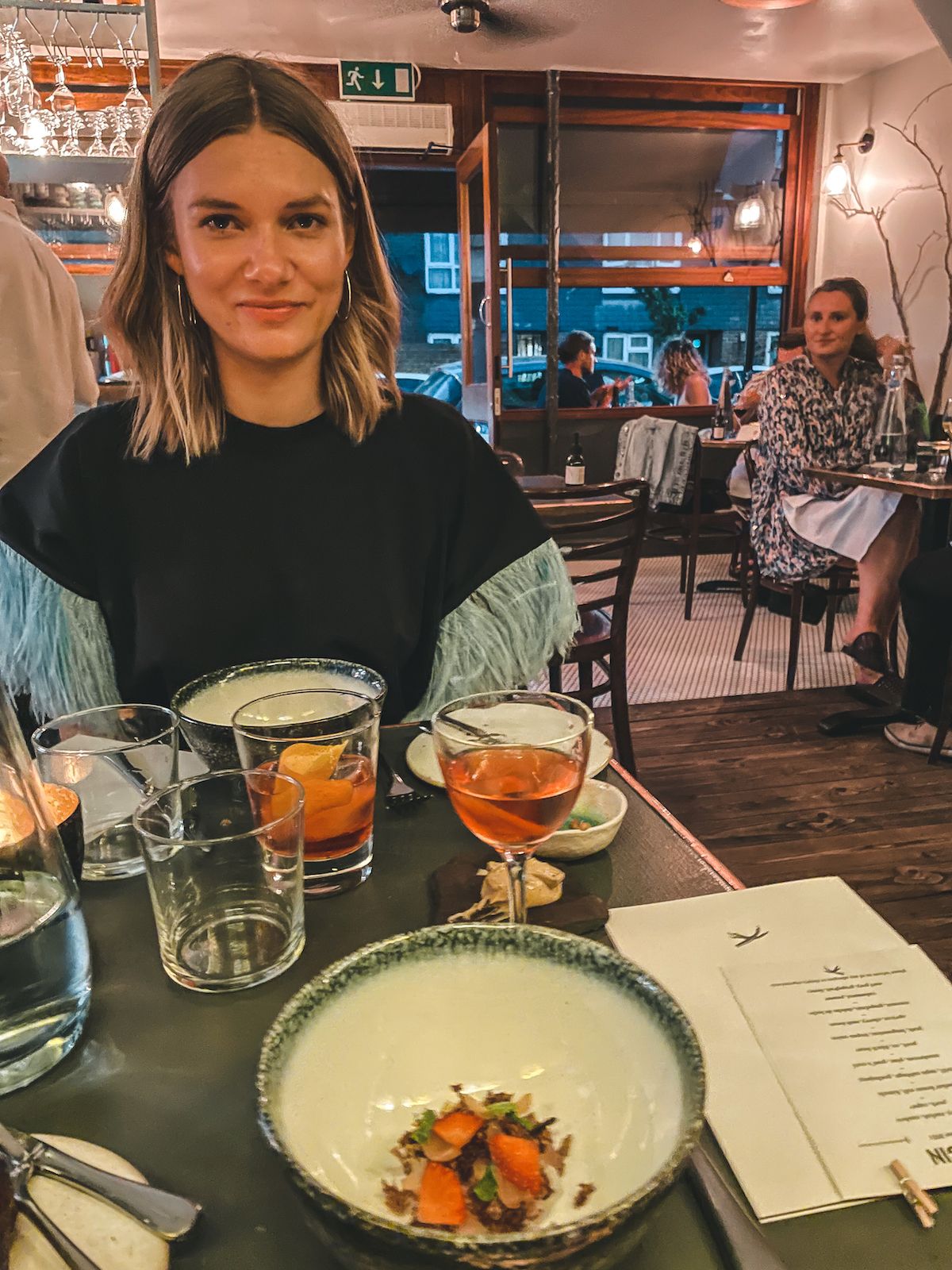 East London local, Katarina, enjoying cocktails and a gourmet meal at a cozy, dimly lit restaurant in Hackney.
