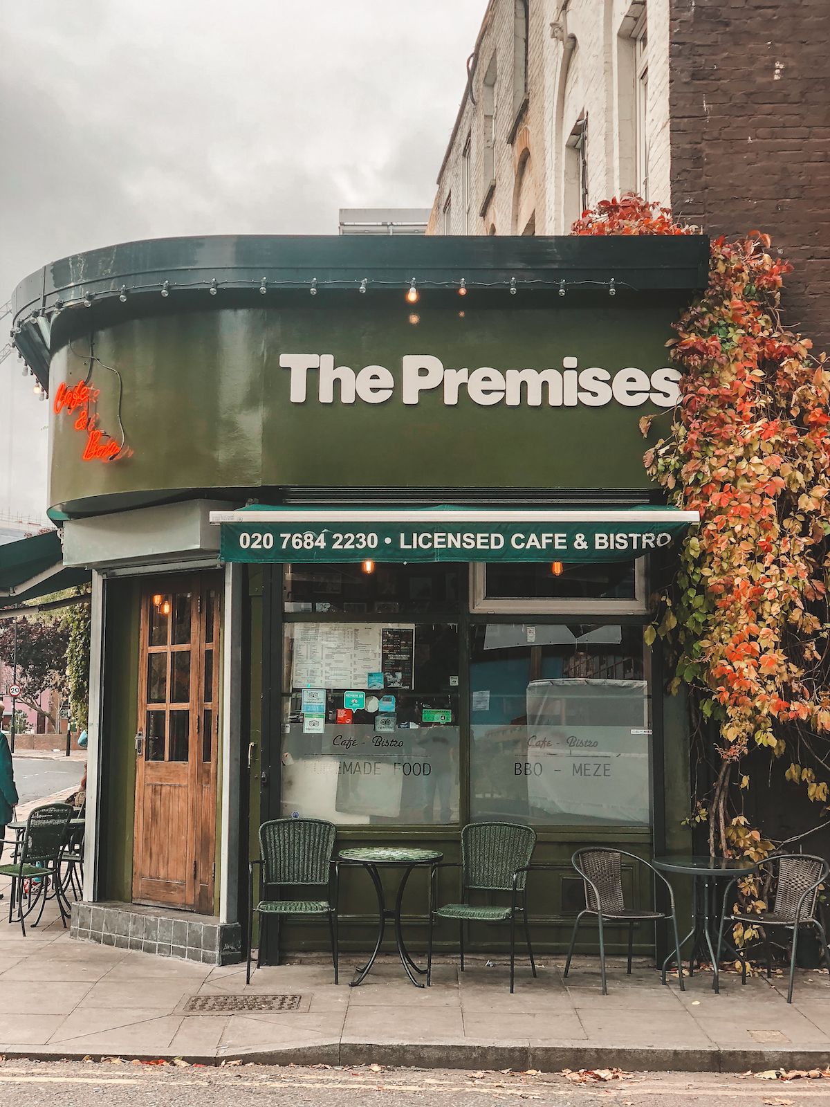The green storefront of The Premises Cafe in London, with an outdoor seating area covered in autumnal vines.