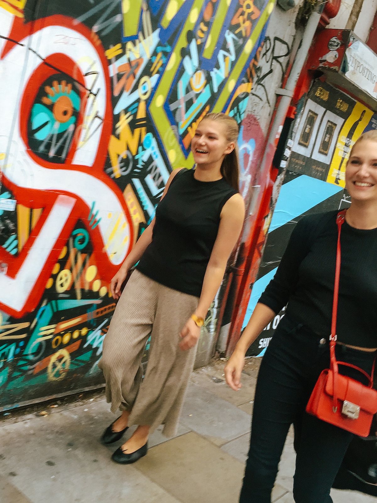 Cec and Katarina walking along walking past a colourful graffiti wall in Shoreditch.