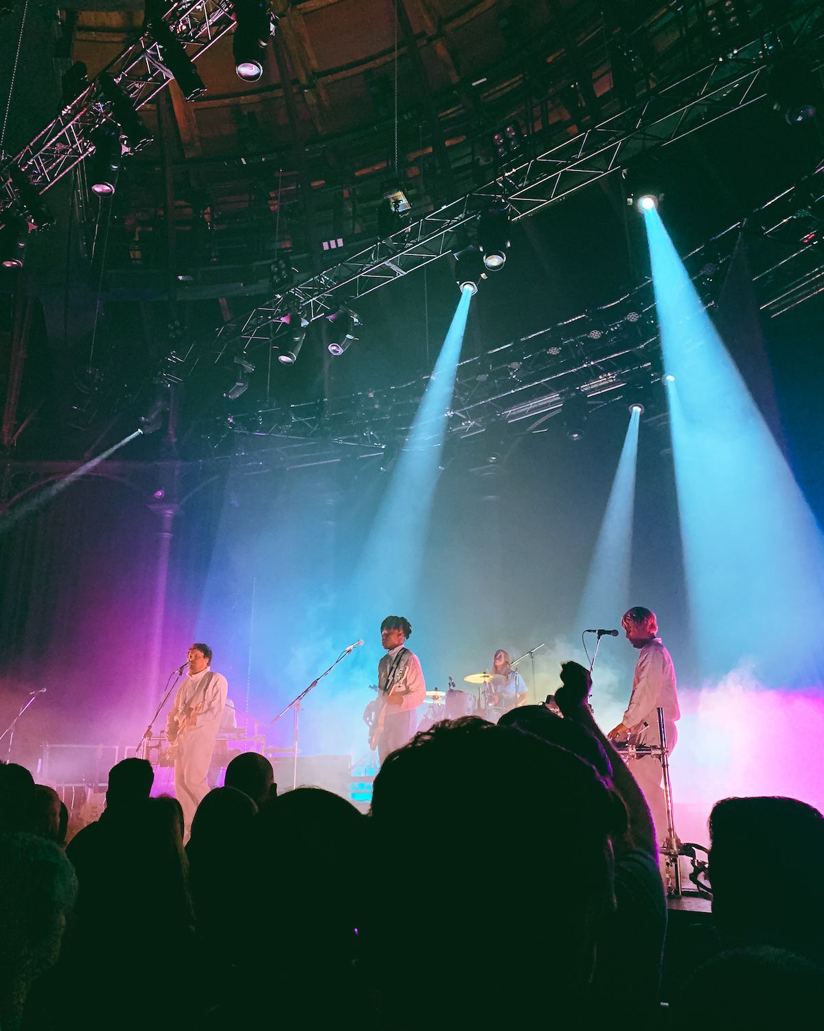 A vibrant concert scene at Roundhouse with the musicians of Metronomy under colourful stage lighting, with an engaged crowd in the foreground. 