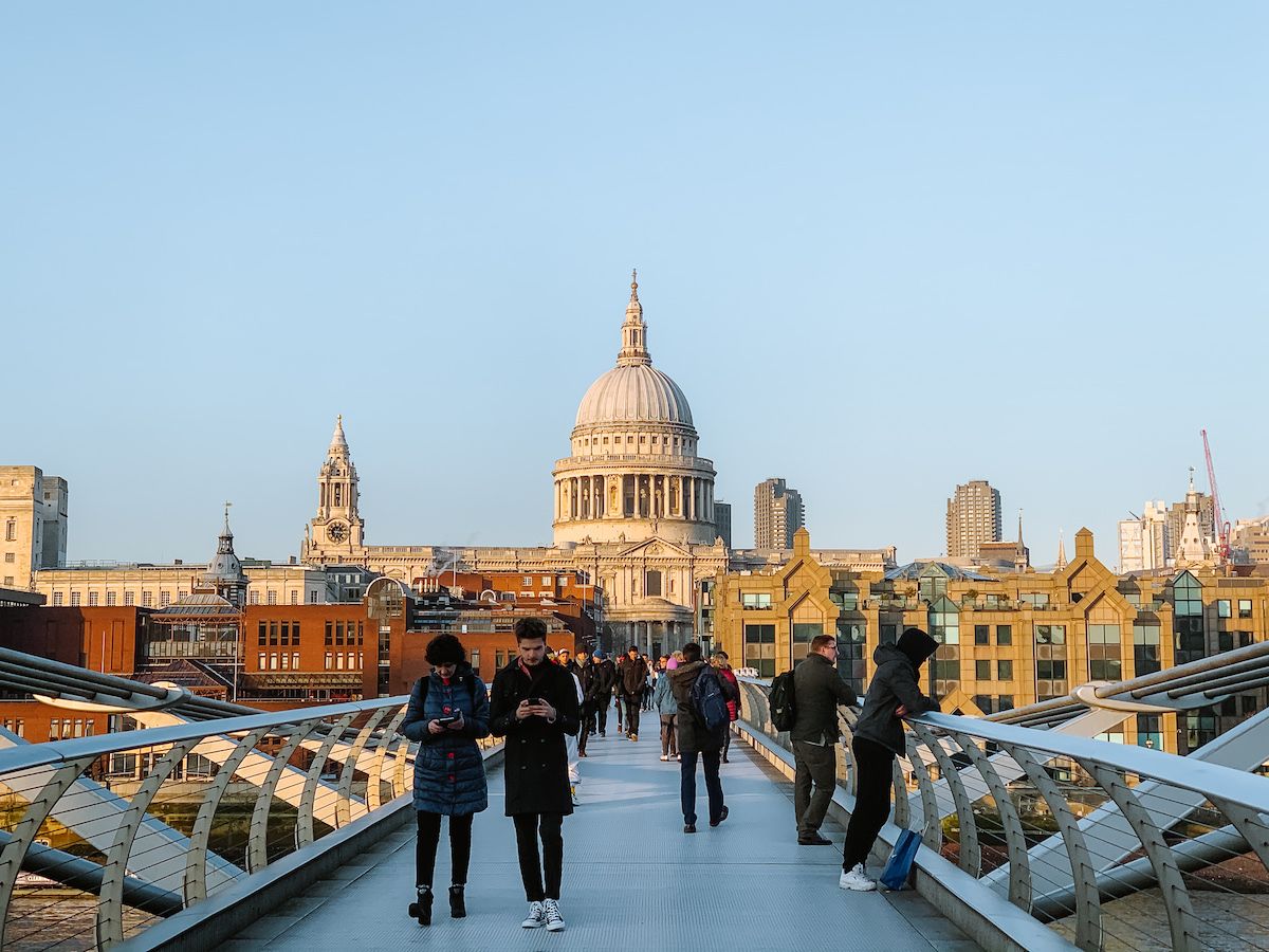 People walking across the modern Millenium Bridge with St. Paul’s Cathedral visible in the background.