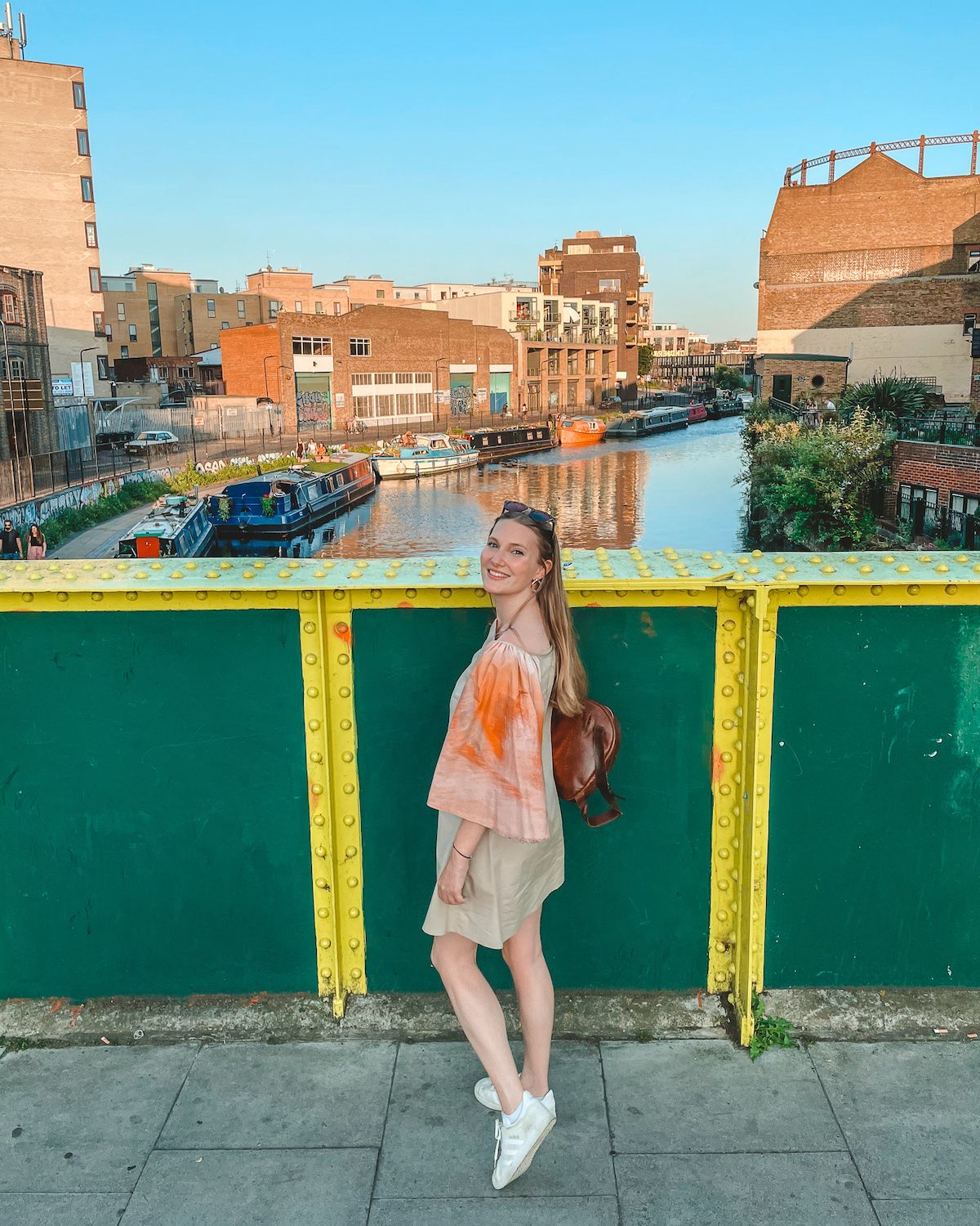 Cec standing against a yellow and green bridge overlooking canal boats and brick buildings in East London.
