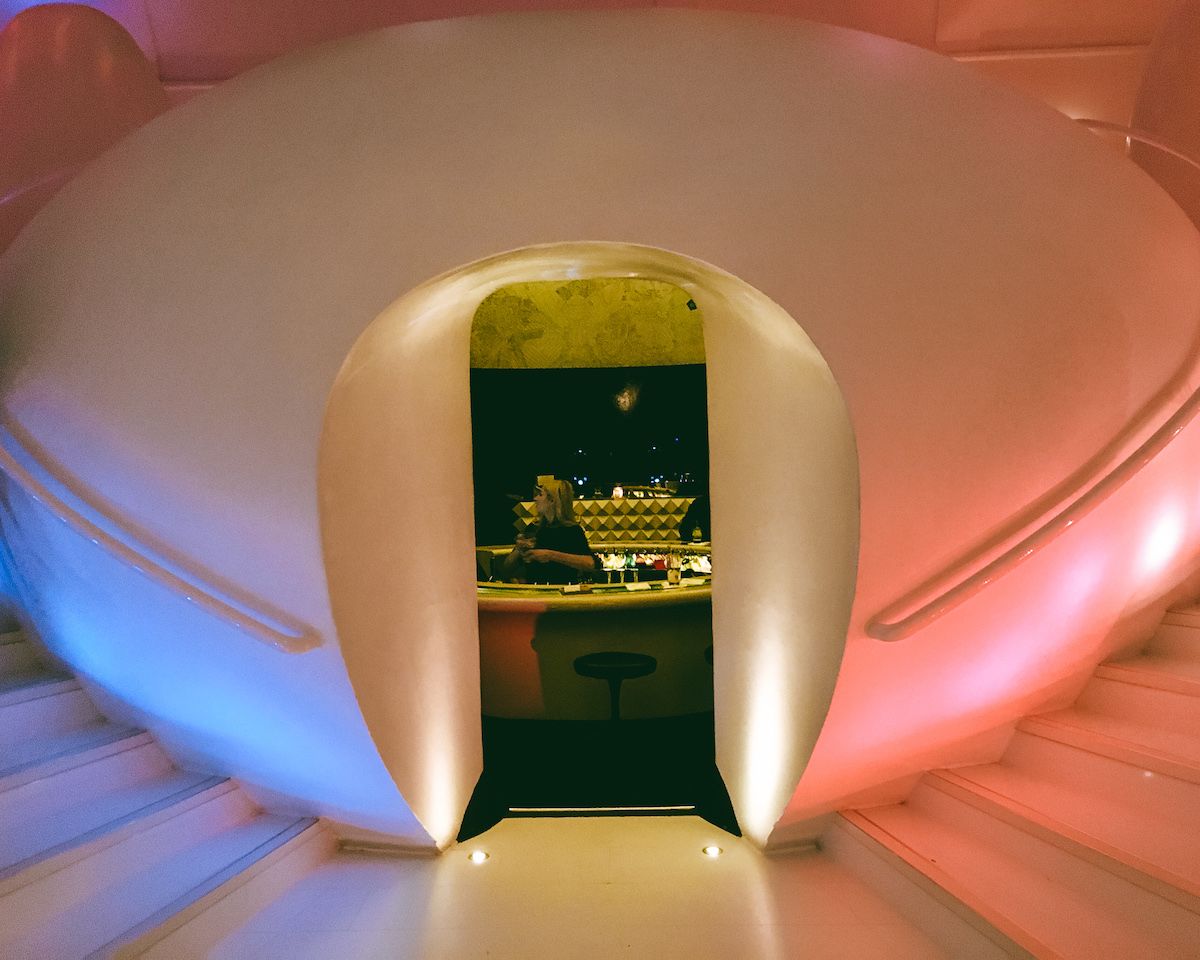  A rounded, pod-like white entrance glowing in pink and blue lights, leading to the spaceship-inspired bar at Sketch London.