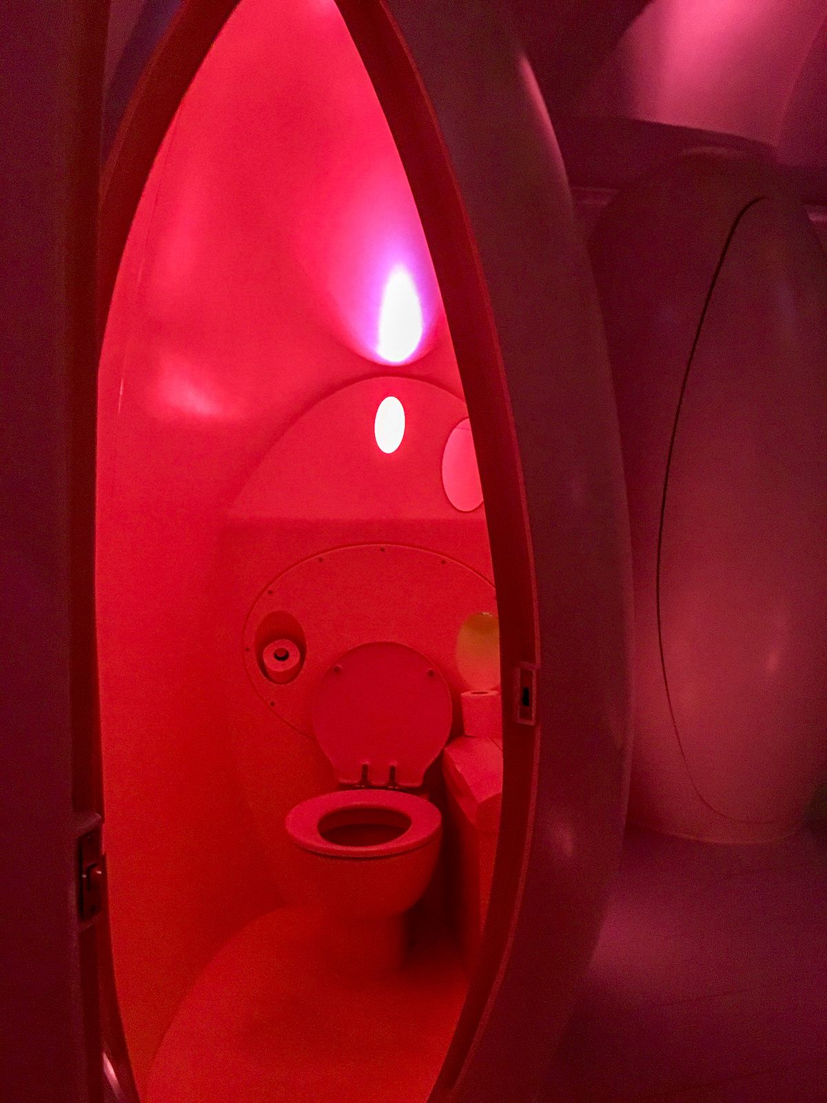 A futuristic bathroom pod bathed in soft red lighting inside Sketch London.