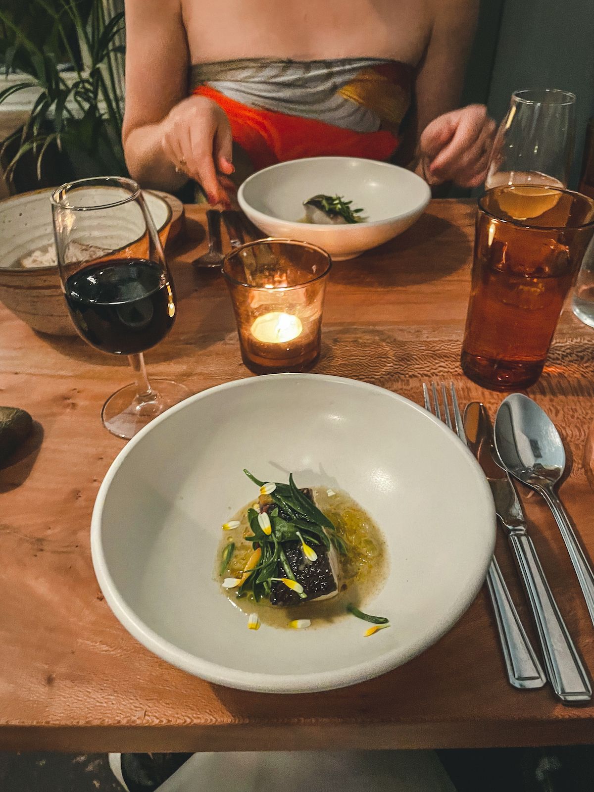 A cozy dinner scene at Casa Fofo with an elegantly plated dish, a glass of red wine, and a warm candle glow.