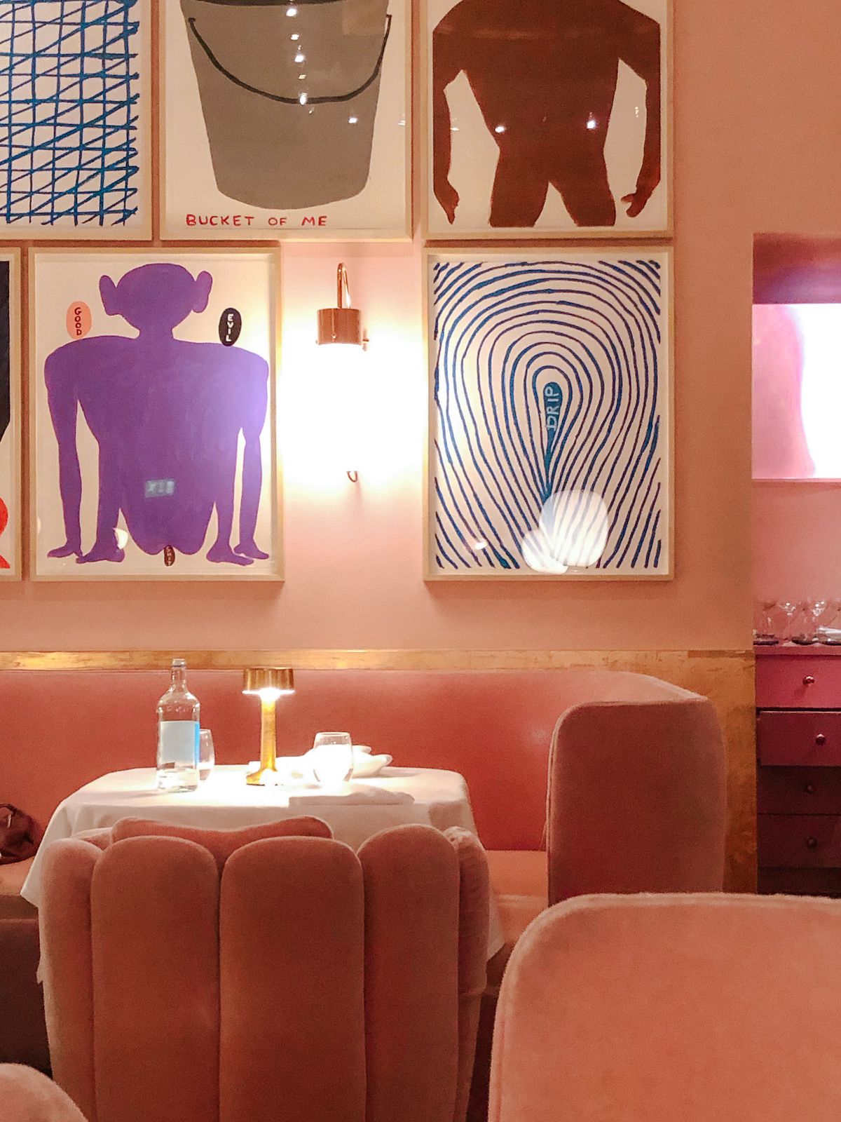 A cozy pink booth with a table set for two, framed by contemporary David Shrigley artworks on the wall.s