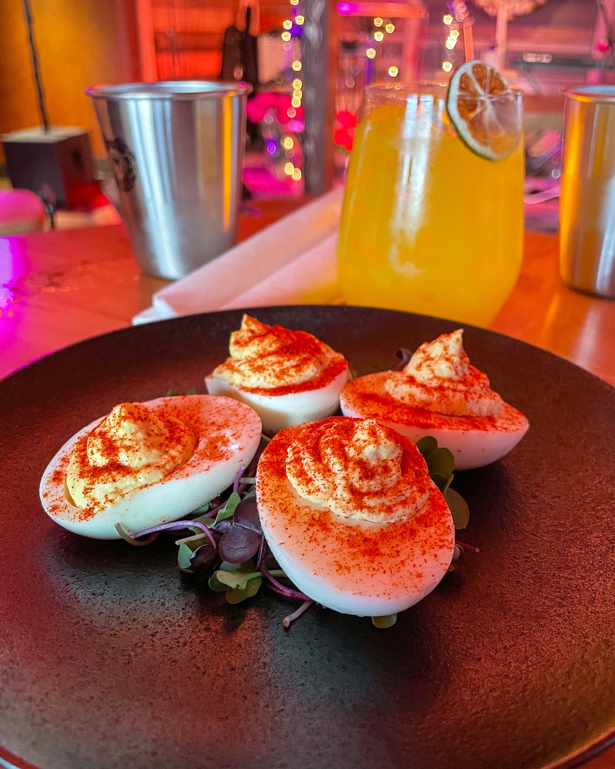 Paprika-topped devilled eggs on a black plate, paired with a yellow cocktail at Mateada.