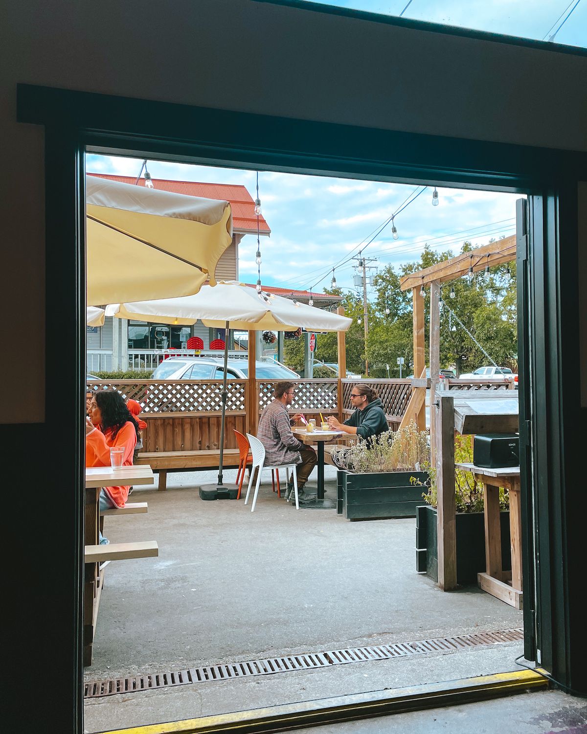 View of Cassette’s outdoor patio with guests dining under umbrellas and string lights, seen from inside the restaurant.