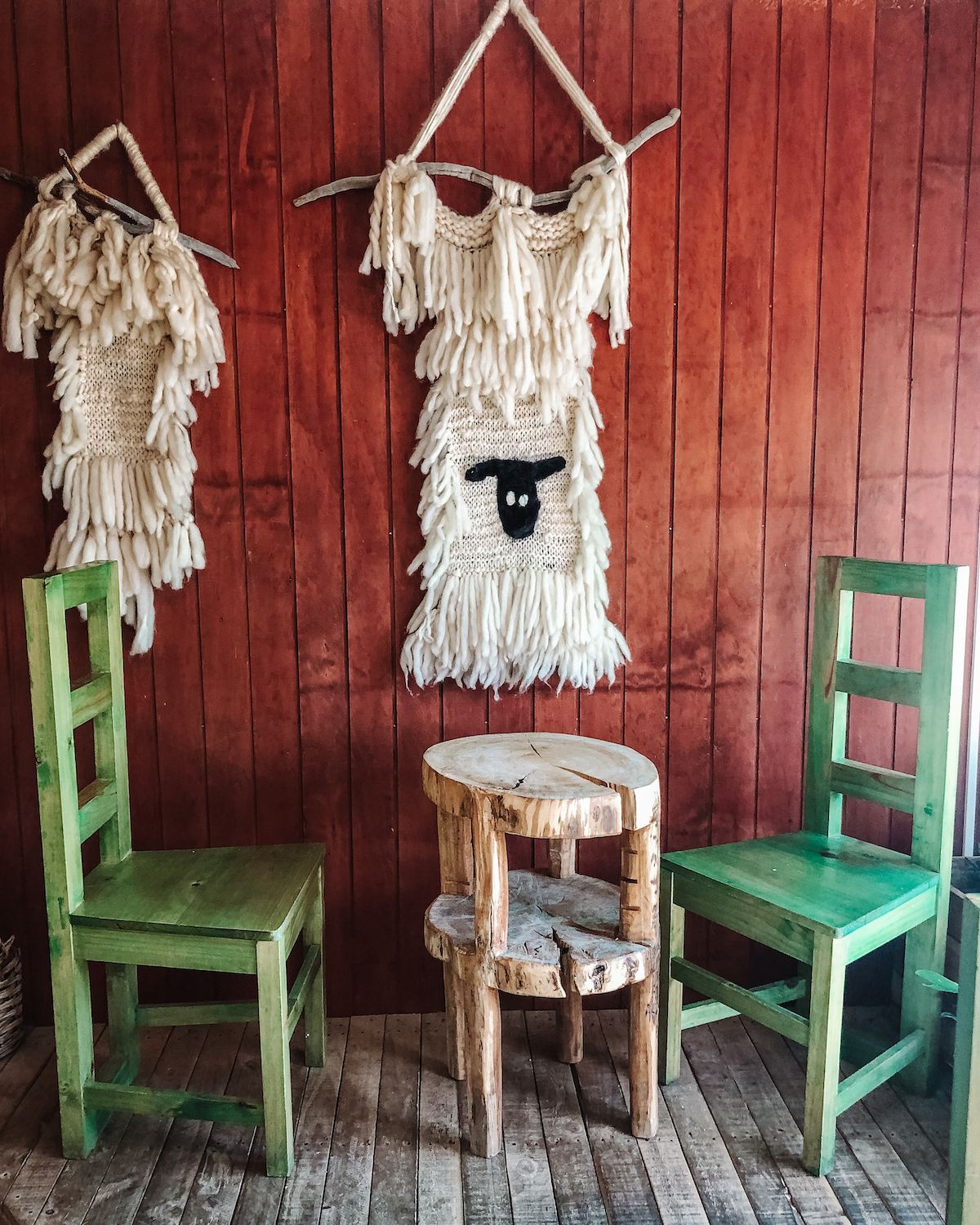 Rustic interior of Cafe Artimana with two green chairs, a wooden table, and woven wool wall art.