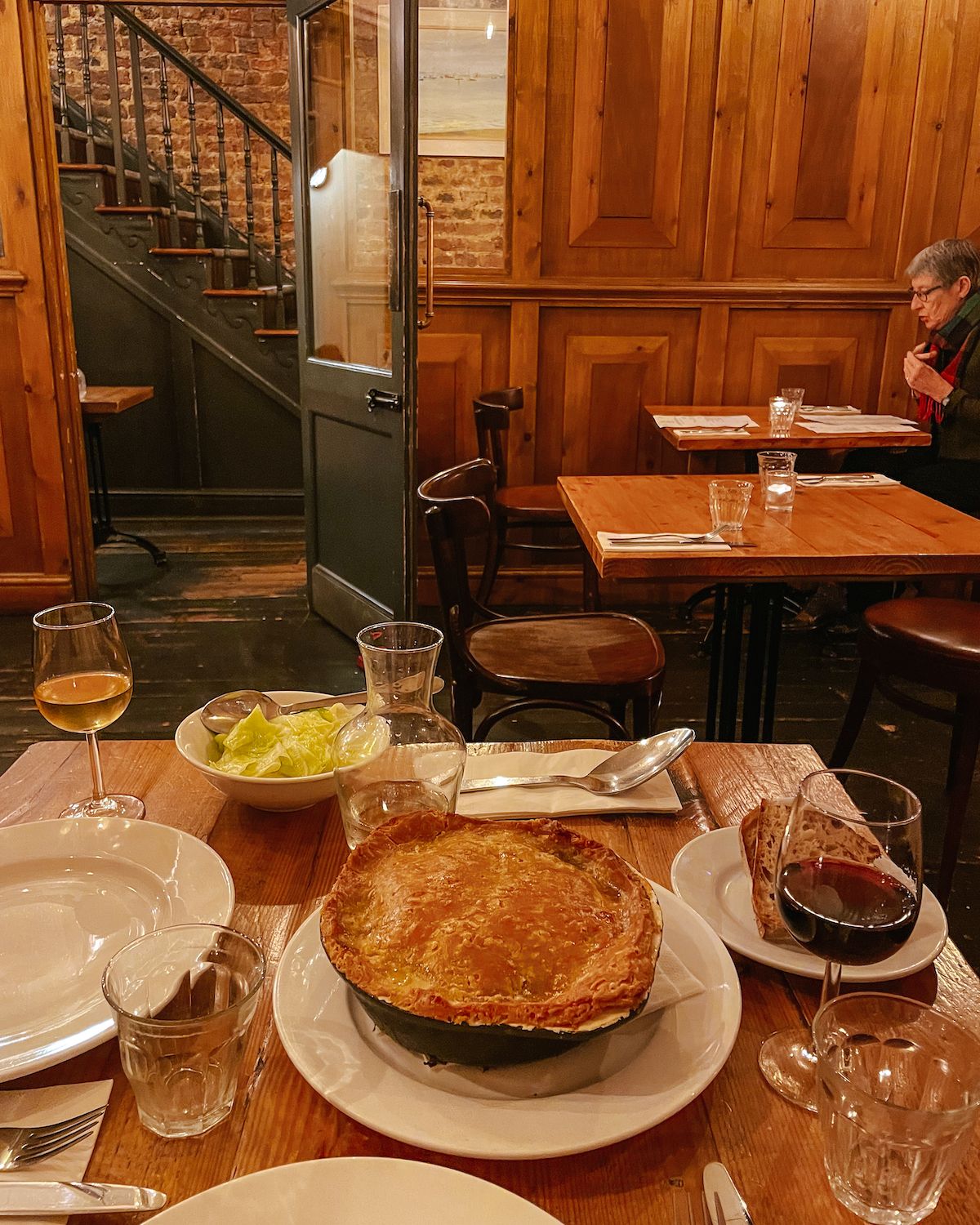A hearty golden-crusted chicken pot pie on a wooden table, served with wine and rustic bread in the warmly lit Clarence Tavern.