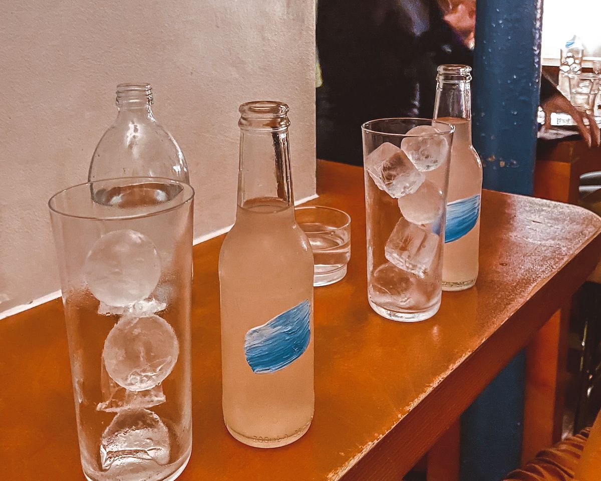 Minimalist glass bottles with artistic blue labels, served with ice-filled glasses in unique shapes.
