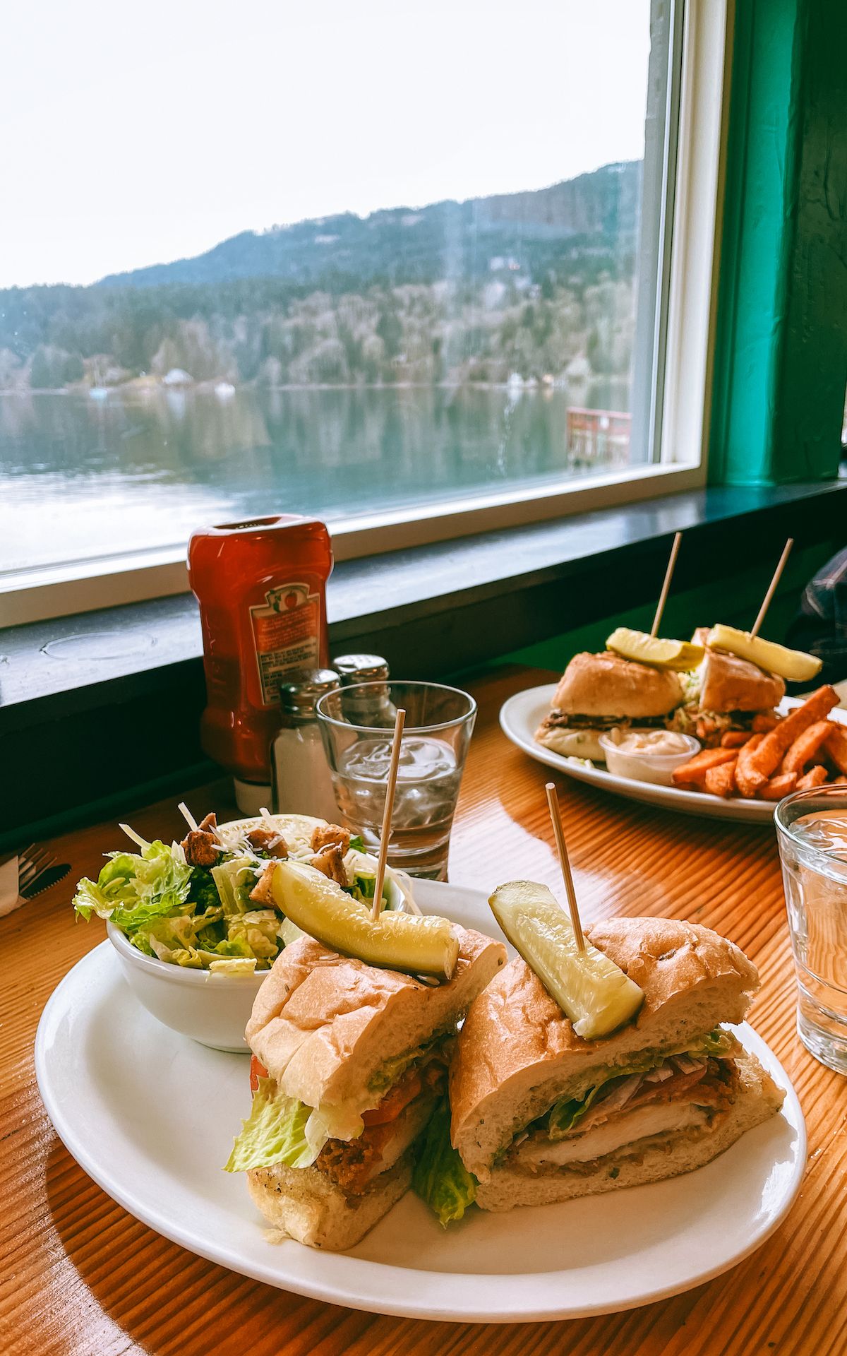 Chicken sandwich with a pickle garnish and salad, served by the window with scenic waterfront views at Rock Salt Restaurant.
