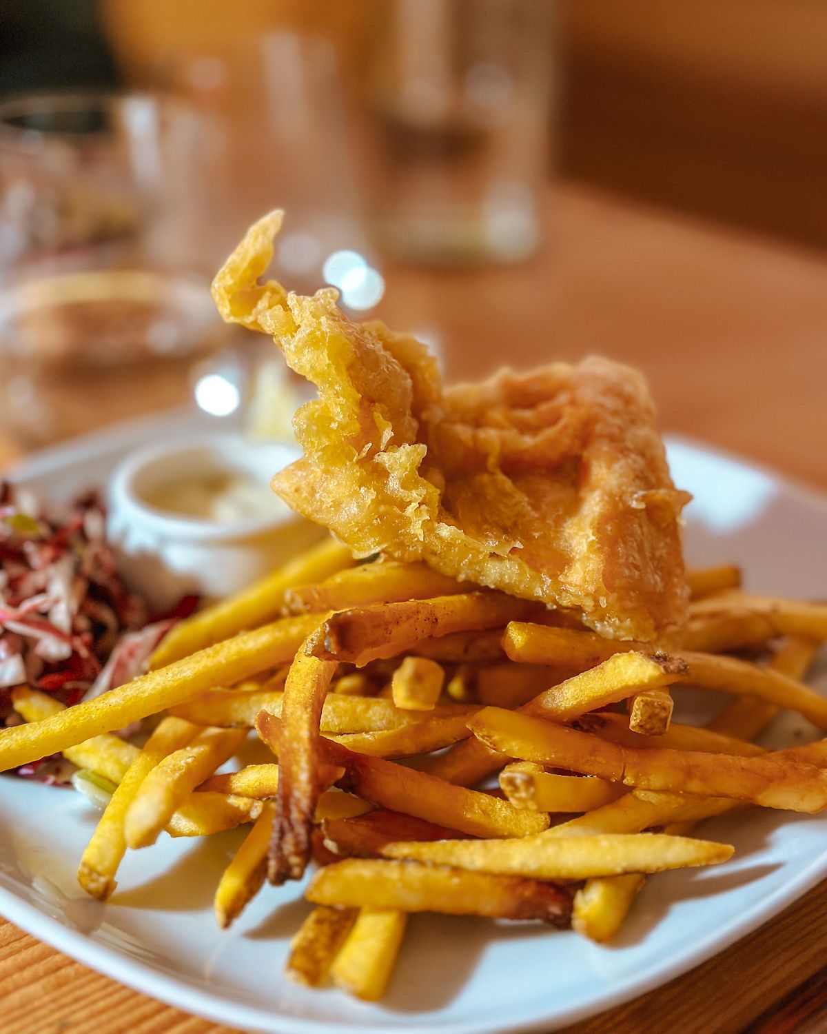 Close-up of crispy salmon fish and chips with a side of creamy tartar sauce and slaw, served on a white plate at Off the Hook.