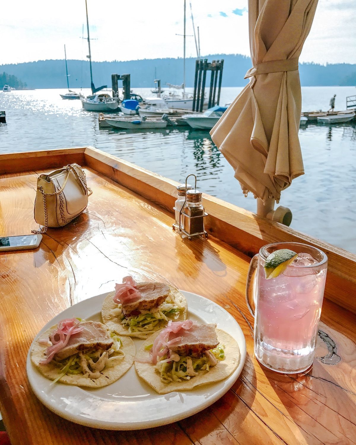 Plate of fish tacos with a pink drink on a table overlooking Montague Harbour.