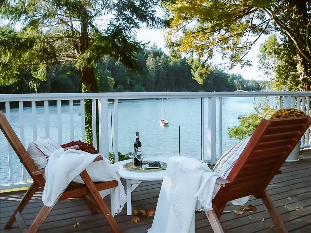 Two patio chairs and a table with a bottle of wine and wine glasses overlooks Whaler Bay at Waterfront Staycation B&B.