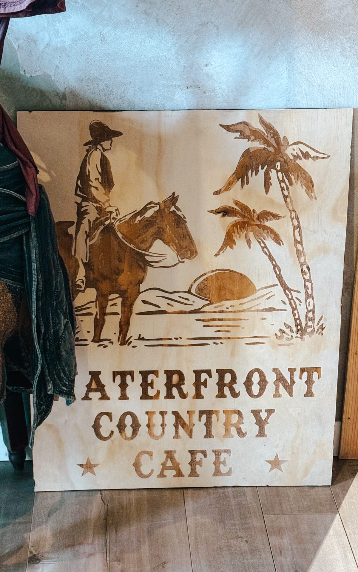 Wooden sign for Waterfront Country Cafe, featuring a cowboy on horseback on an island in a rustic design.