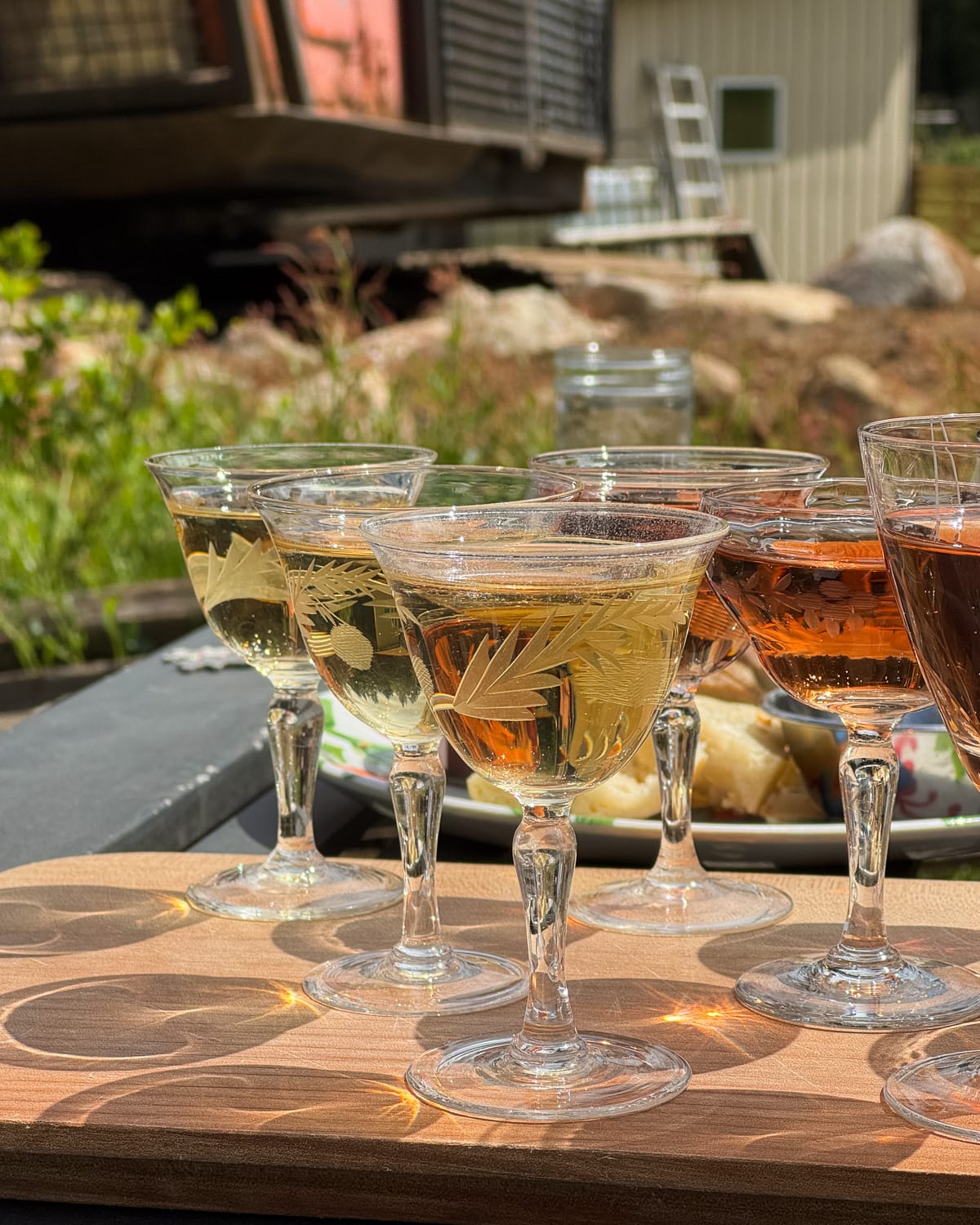 Close-up of a cider tasting flight with etched vintage glasses filled with golden, amber, and red hues, gleaming in the sun at SouthEnd Farm on Quadra Island.