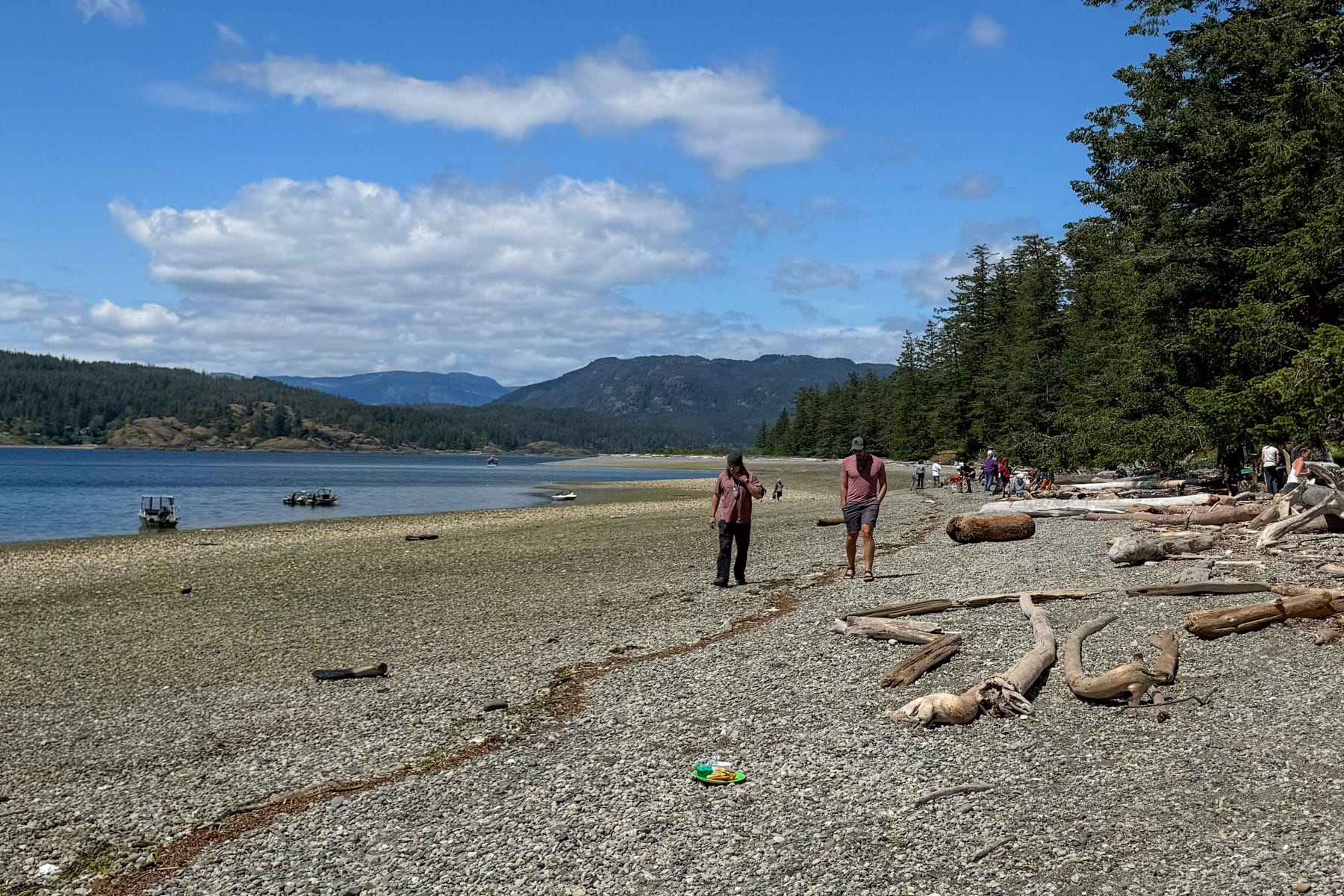 Scenic beach at Rebecca Spit Marine Provincial Park with Ari and a friend strolling along driftwood-lined shore with coastal mountains in the distance.