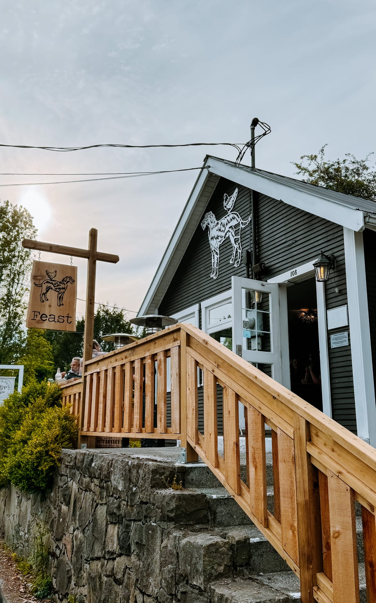 Exterior of Feast restaurant on Salt Spring Island, with wood-railed stairs and signage featuring a dog and chicken logo..