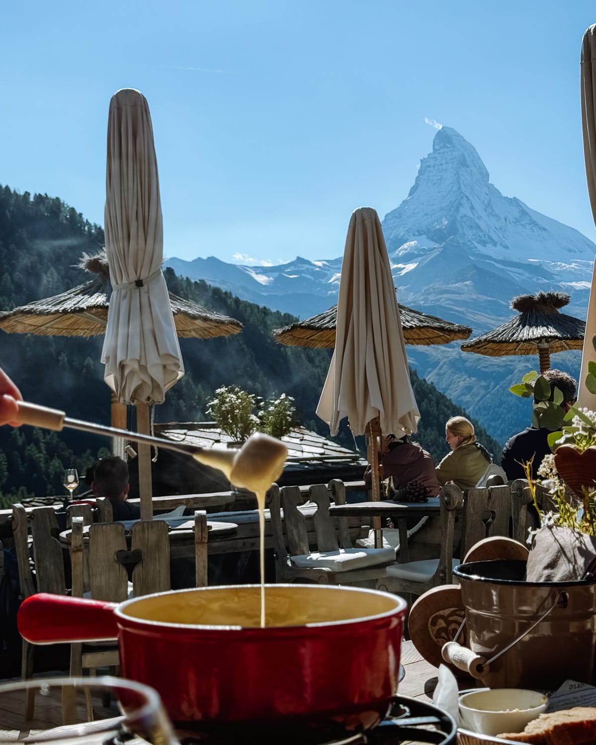  Melting cheese fondue being dipped with bread on a sunny terrace offering a scenic view of the Matterhorn.
