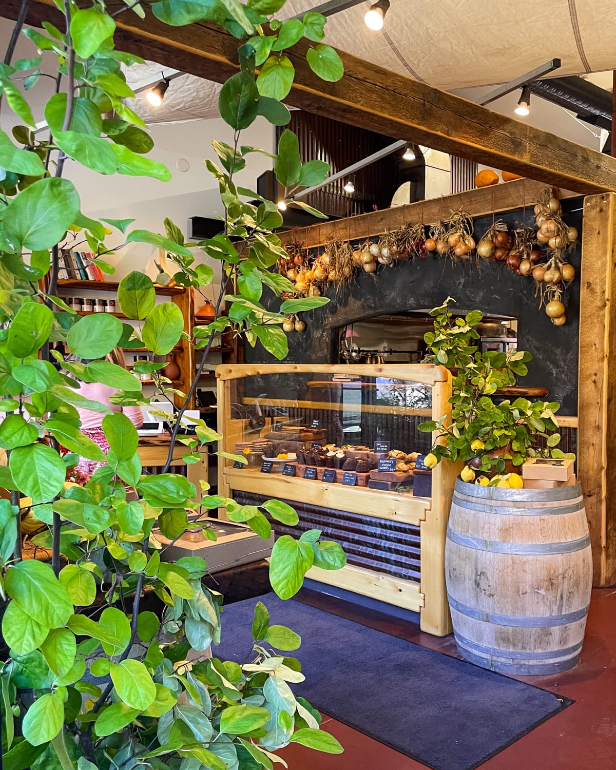 Interior of Woodshed Provisions on Salt Spring Island, featuring a rustic pastry display, hanging onions, and lush potted plants.