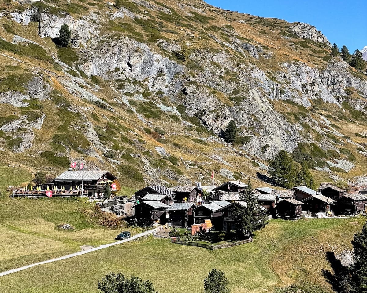  The Rustic mountain village of Zmutt with traditional wooden chalets nestled at the base of steep, grassy mountains.