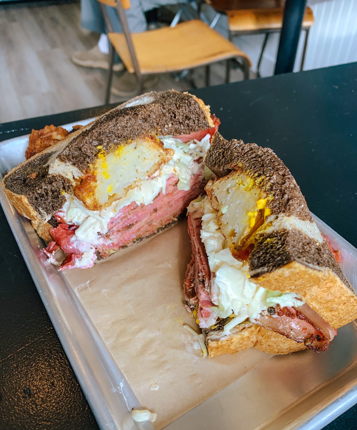 Close-up of Buzzy’s Luncheonette’s smoked meat sandwich on dark rye with coleslaw, latkes and mustard, cut in half.