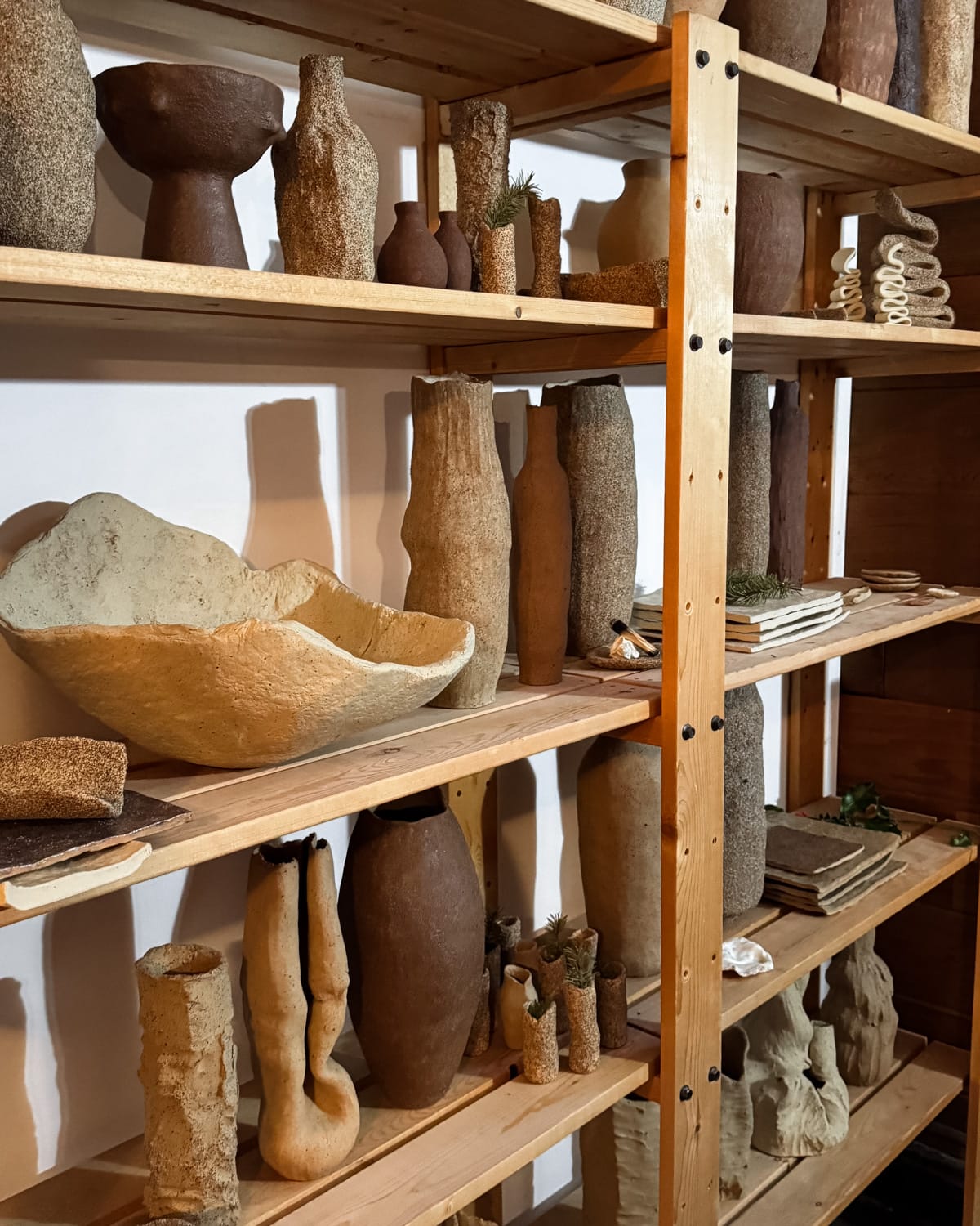 Wooden shelves holding handcrafted ceramic and clay pottery in various shapes and earthy tones.