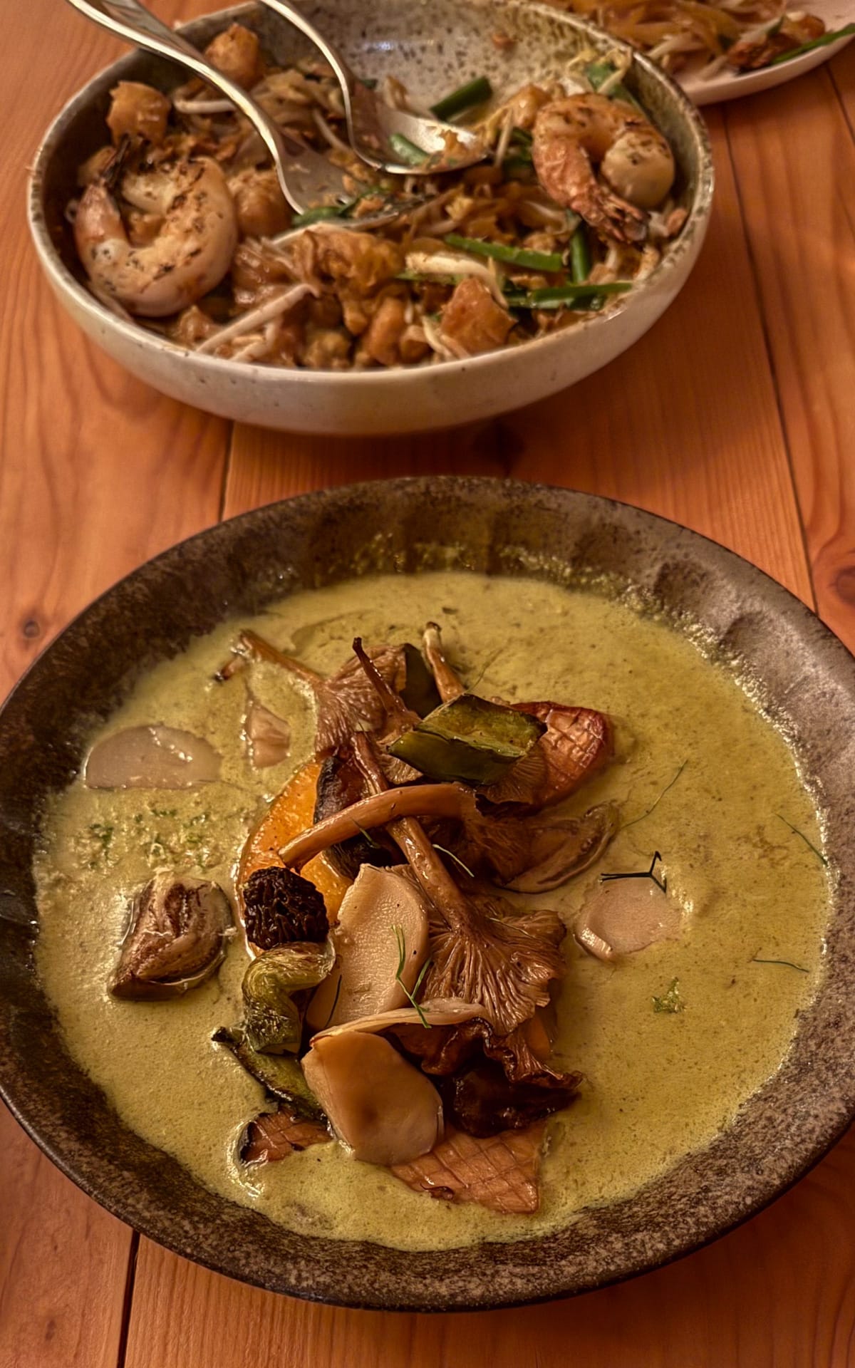 A bowl of rich curry with wild mushrooms, served on a rustic wooden table at Lola