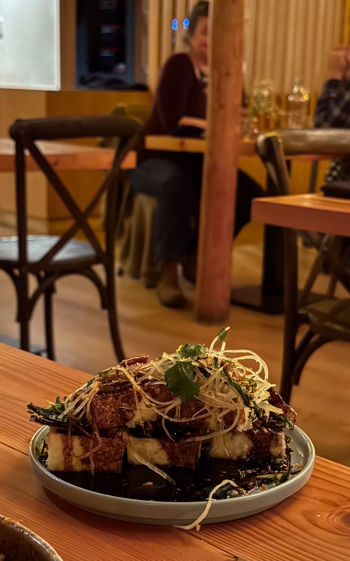 A plate of crispy tofu topped with shredded vegetables and fresh herbs, served in Lola's warmly lit dining room.