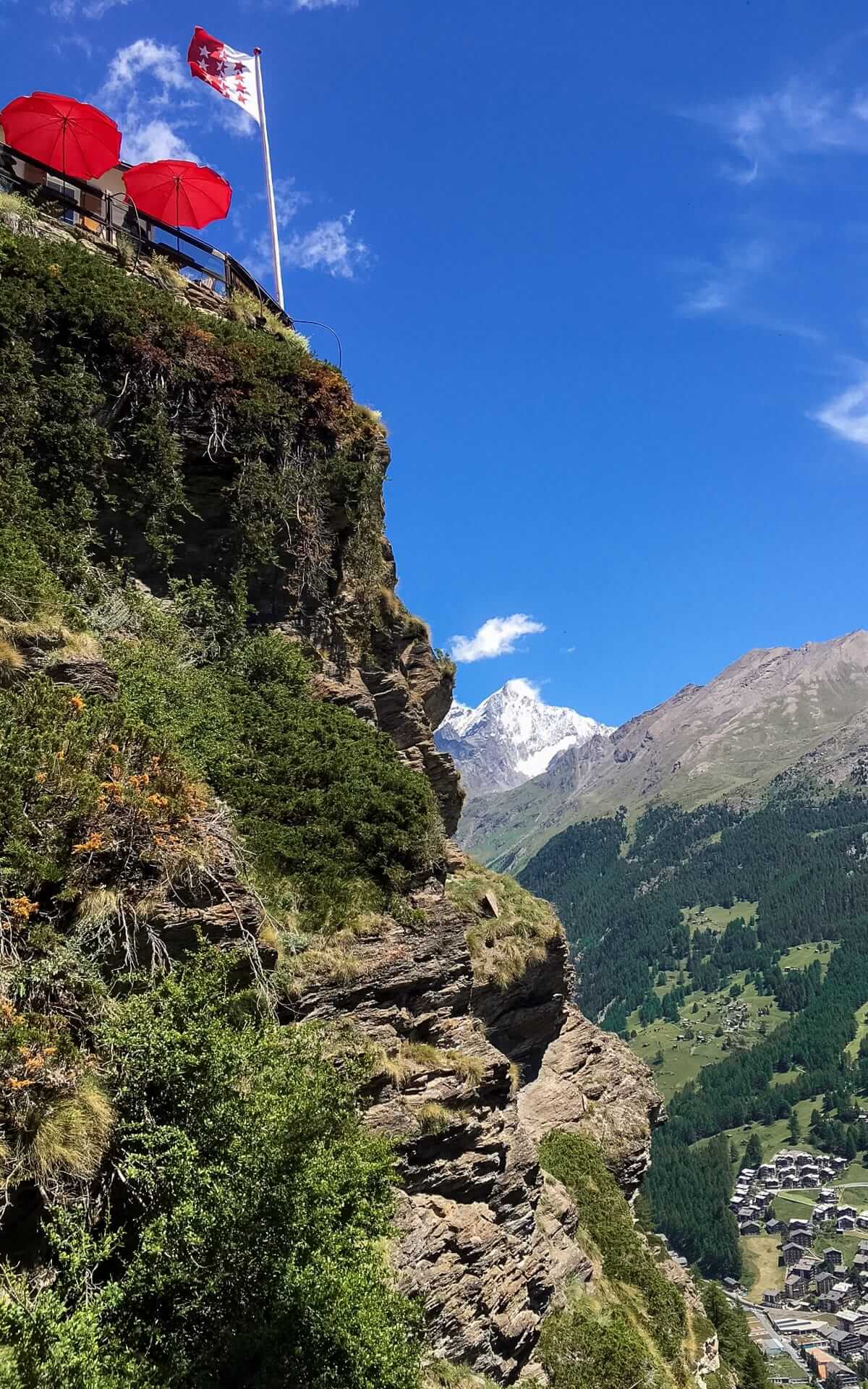 Edelweiss's cliffside terrace with a Swiss flag and red umbrellas offering panoramic views of Zermatt below.