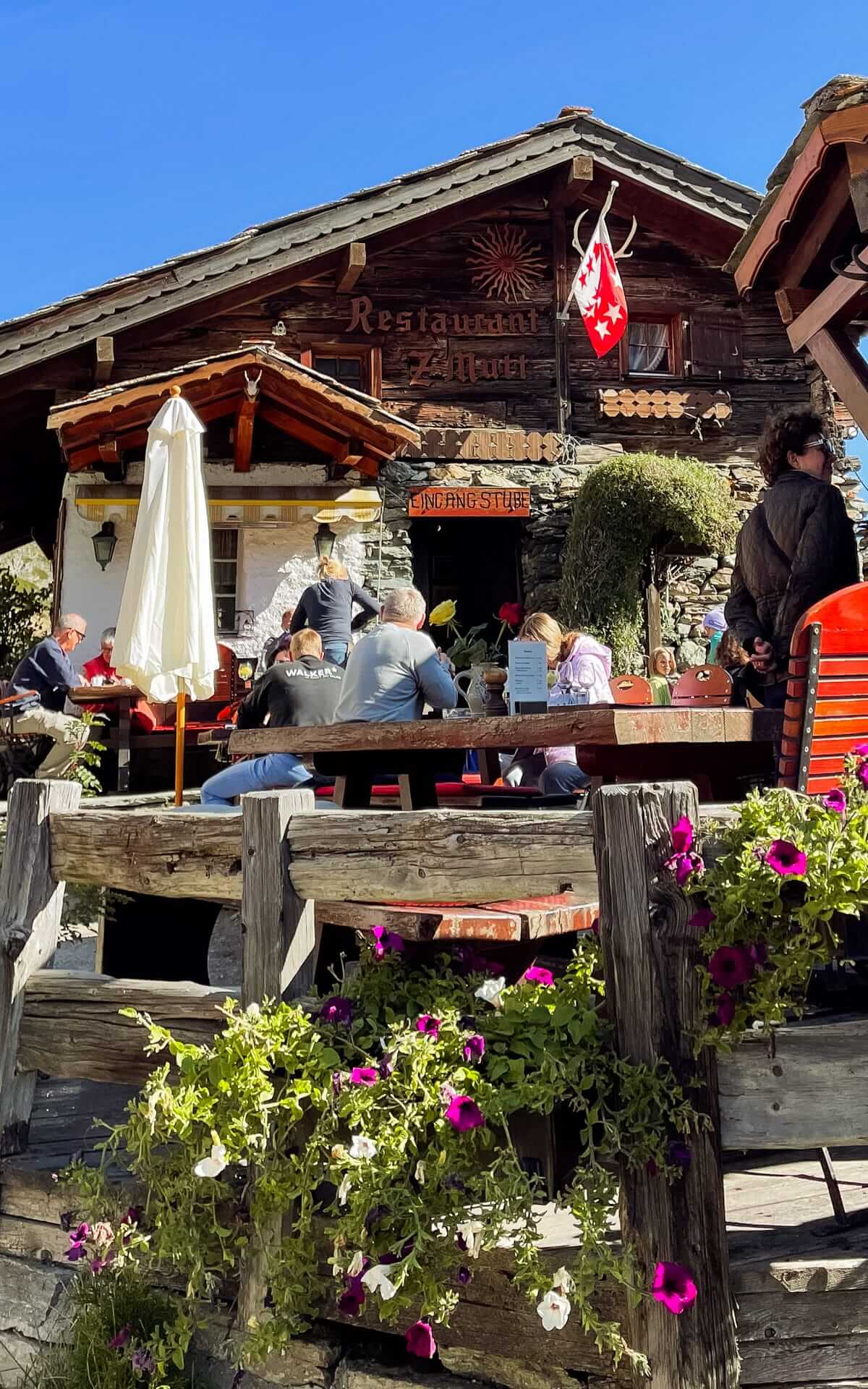 Outdoor seating at Restaurant Z'mutt, surrounded by flowers and Swiss decor, under clear skies.
