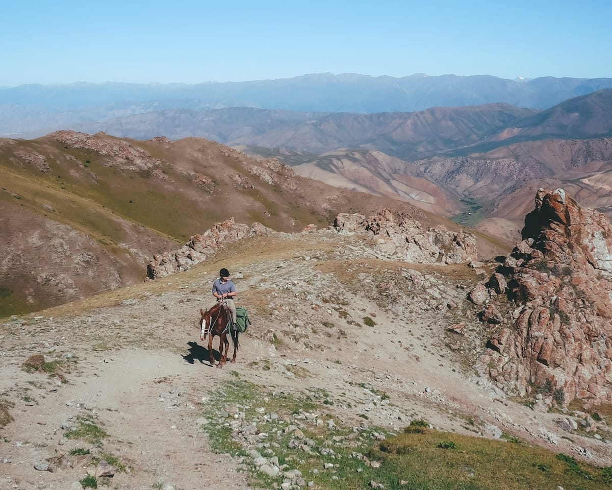 Ari on horseback follows a rugged alpine mountain path on a trek to Song Kul Lake in Kyrgyzstan.