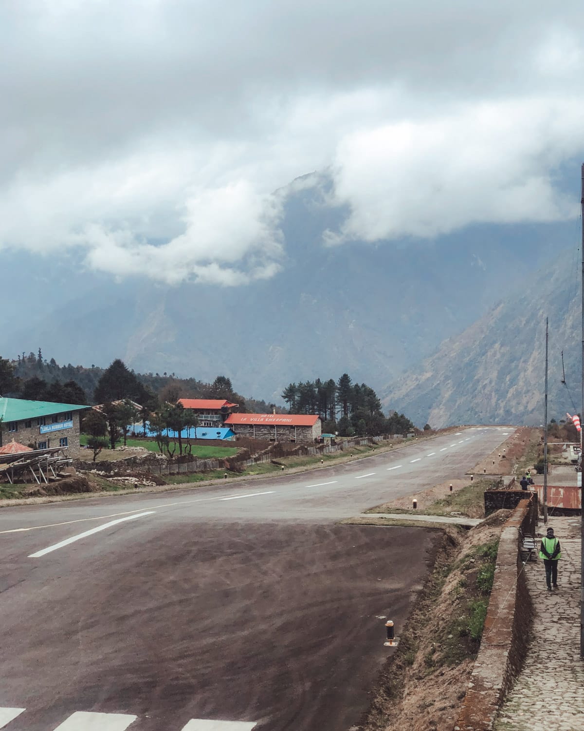 View of Lukla Airport's short runway with a cliff drop off surrounded by misty mountains.
