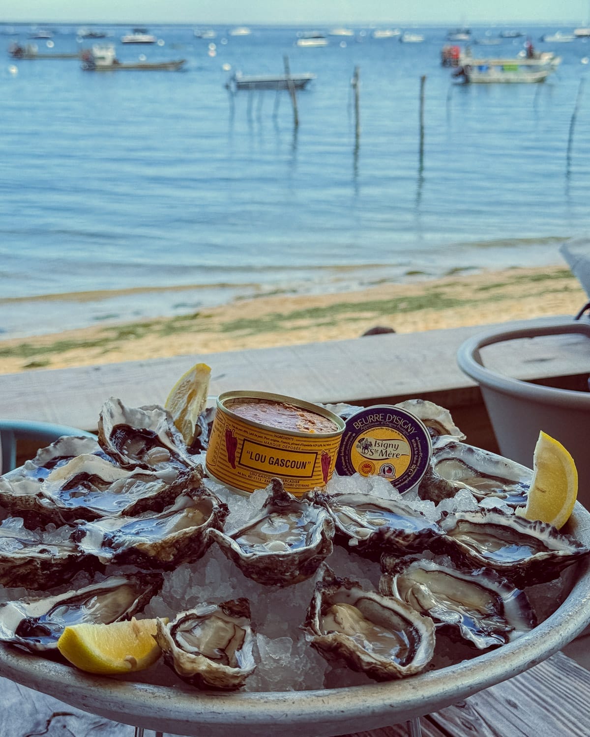 A platter of fresh oysters on ice, served with lemon wedges, pâté, and butter, overlooking the blue waters of L'Herbe..