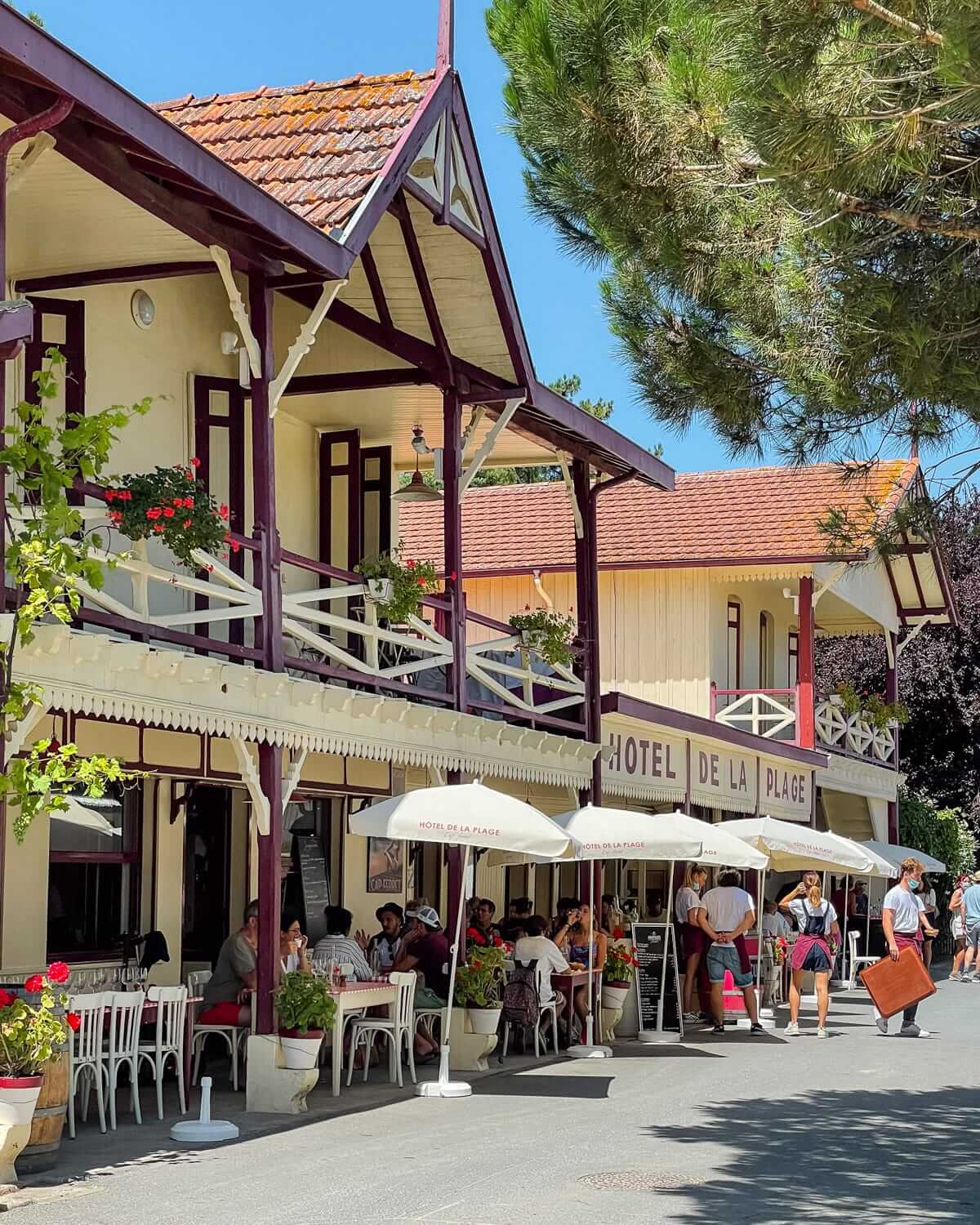 The charming Hôtel de la Plage in L'Herbe, with guests dining under cream umbrellas on a sunny day.