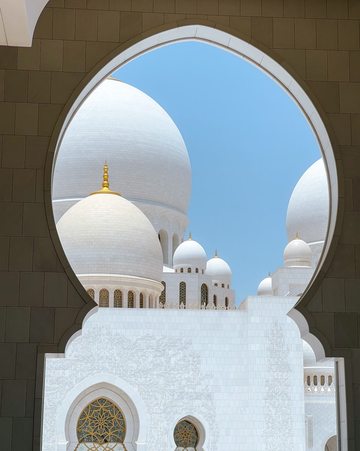 White domes of the Sheikh Zayed Grand Mosque in Abu Dhabi framed by an ornate archway.