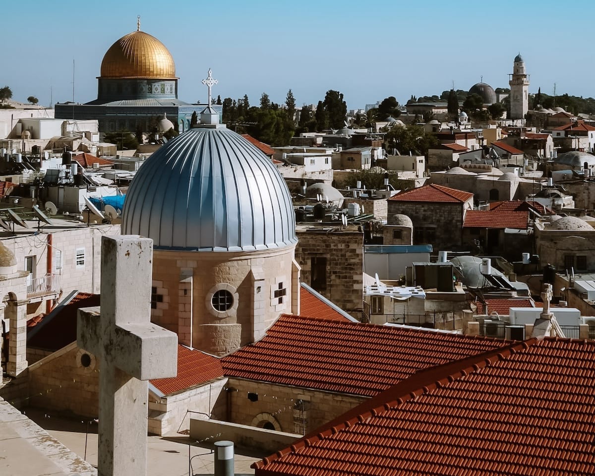 The Dome of the Rock and church domes rise above historic stone rooftops in the Old City of Jerusalem.