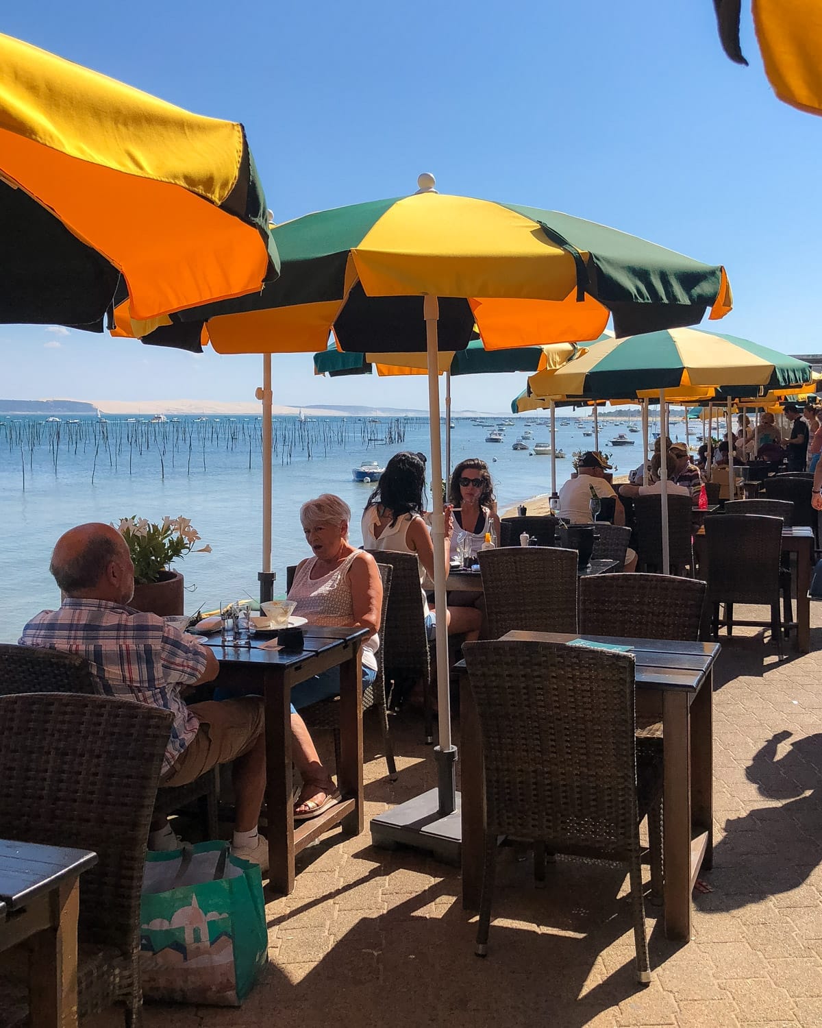 Diners enjoy a meal under green and yellow umbrellas at a L'Escale overlooking the Bassin d'Arcachon.