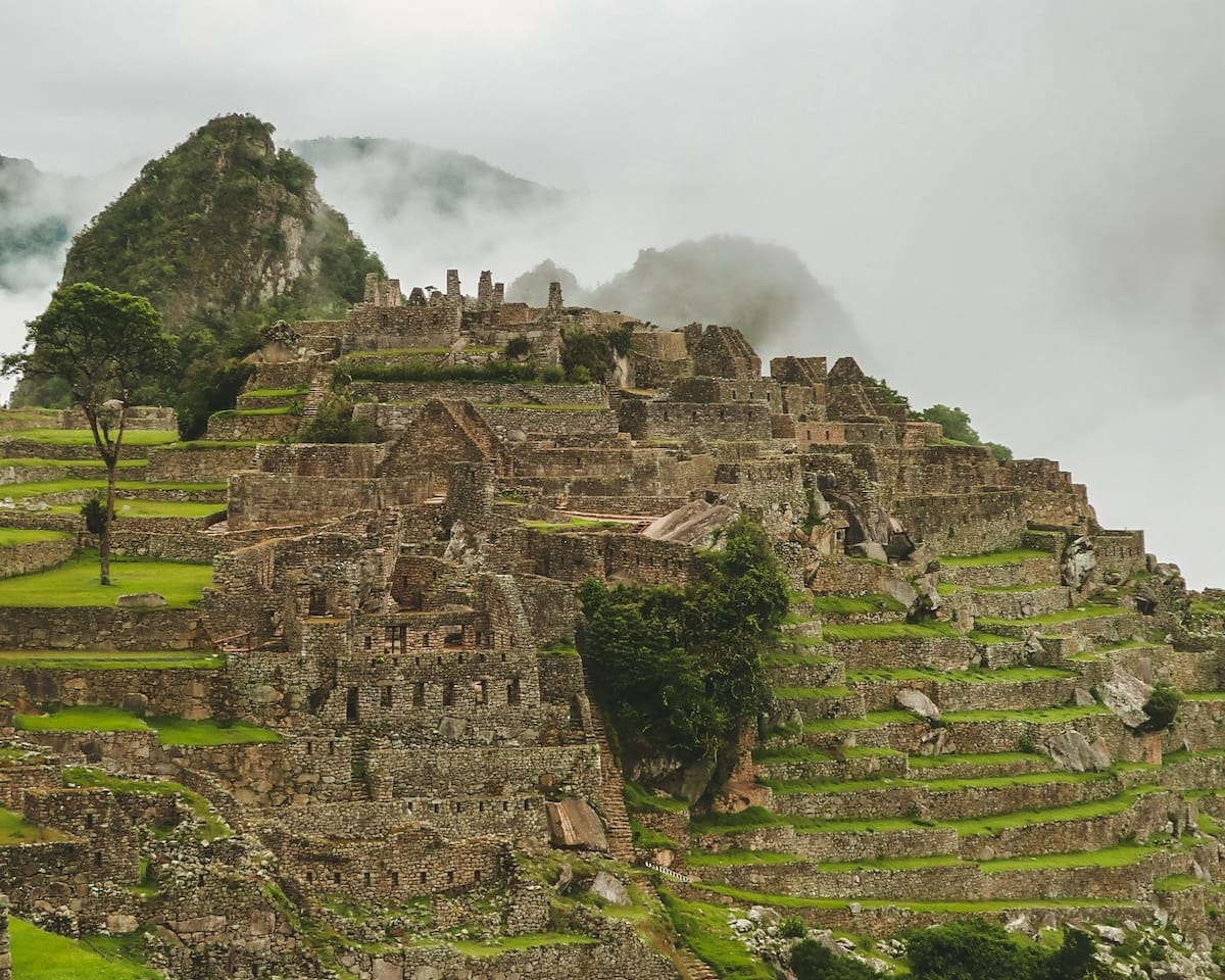 Ancient stone ruins of Machu Picchu rise above cloud forest, with mist clinging to steep peaks in Peru’s Sacred Valley.
