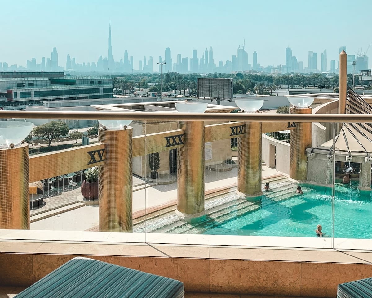 A luxurious pool with golden pillars at Raffles Dubai with and a cityscape view featuring the Burj Khalifa.