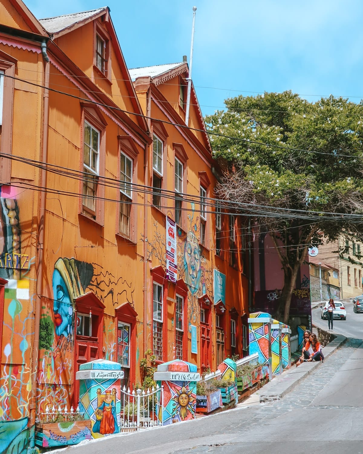  Orange buildings with murals and painted fences along a steep street in Valparaíso.