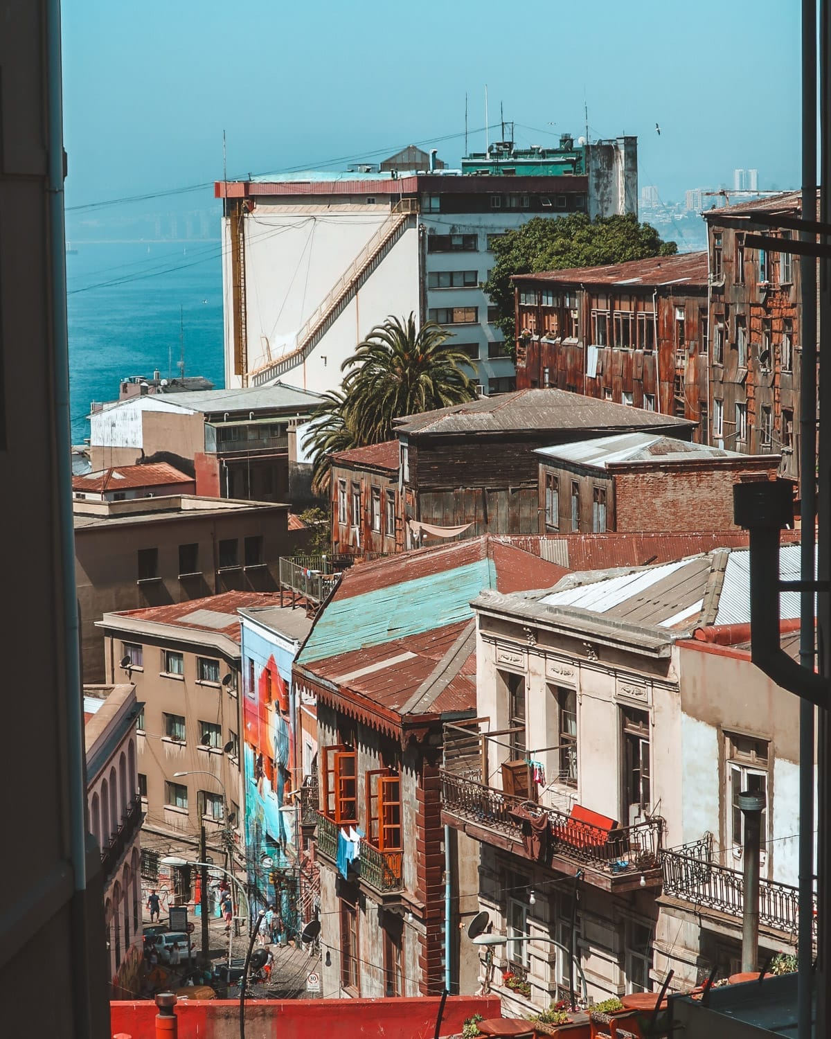View of Valparaíso’s hillside, showing colourful, historic buildings, a large mural, and ocean in the distance.