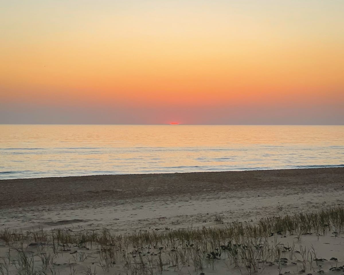A serene sunset over Cap Ferret’s coastline, with the sun dipping below the horizon.