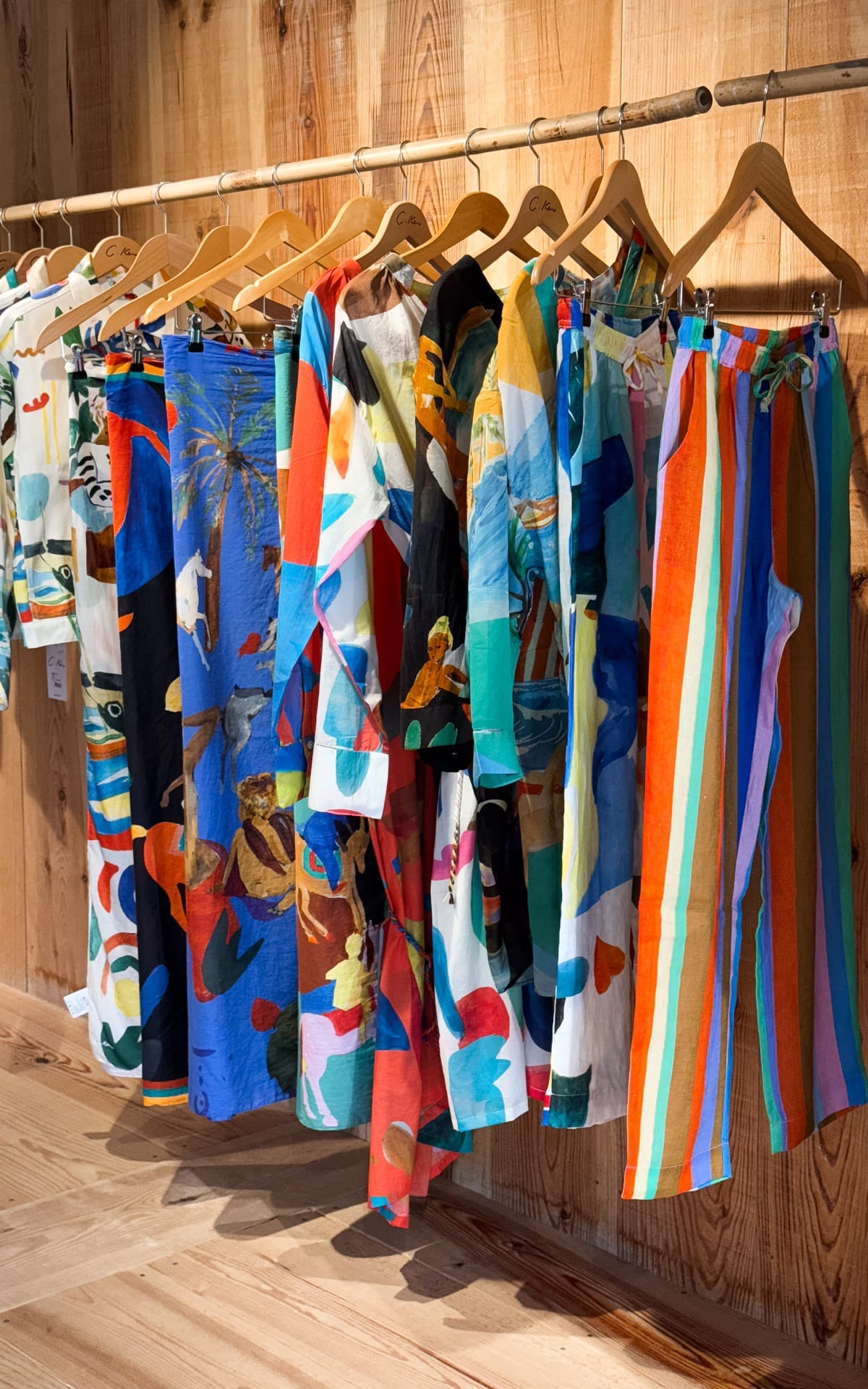 G. Kero clothing boutique displaying vibrant, patterned garments on wooden hangers against a warm, wooden wall.